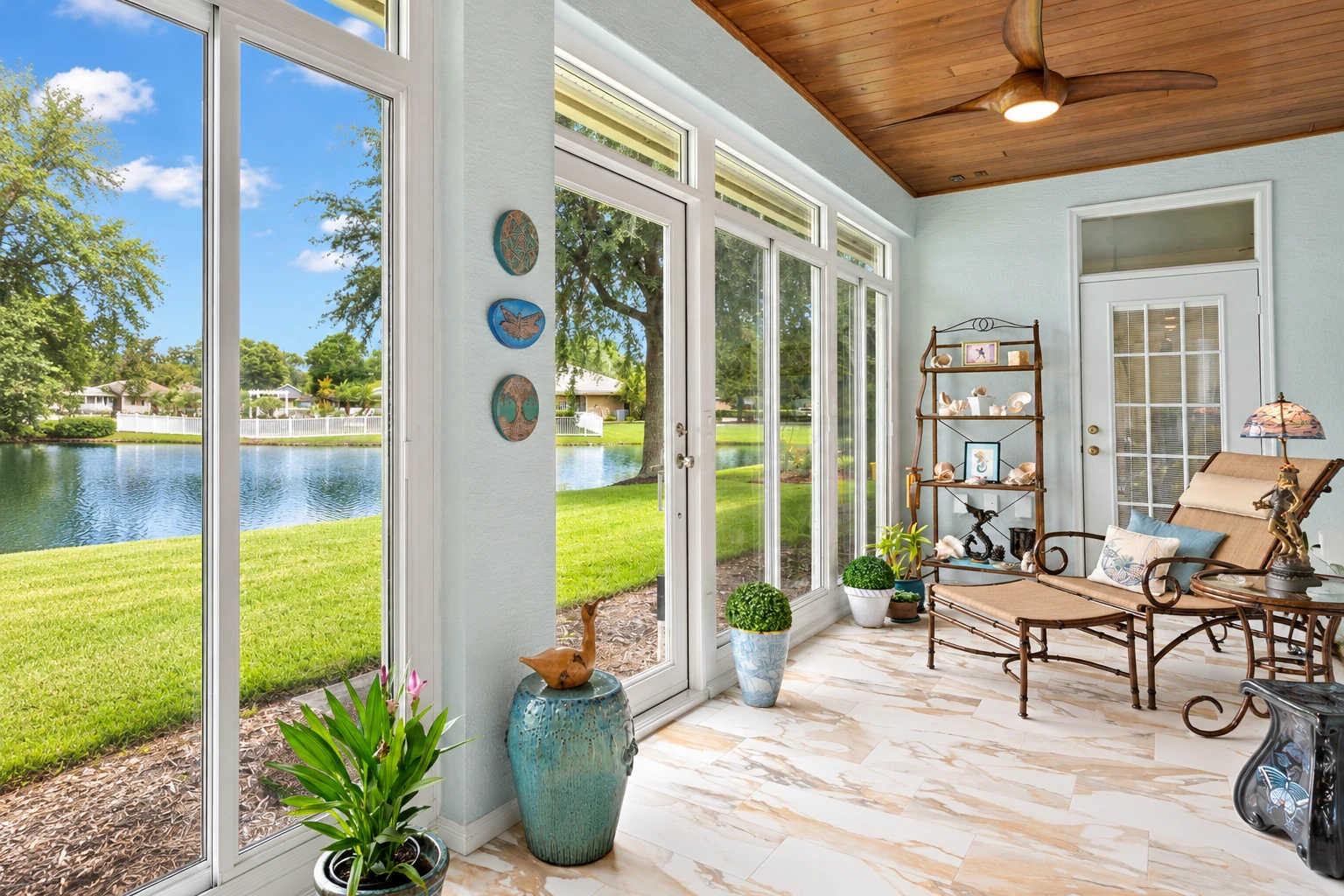 Custom sunroom with tall white-framed windows, a wood-paneled ceiling, and seating beside a pond.