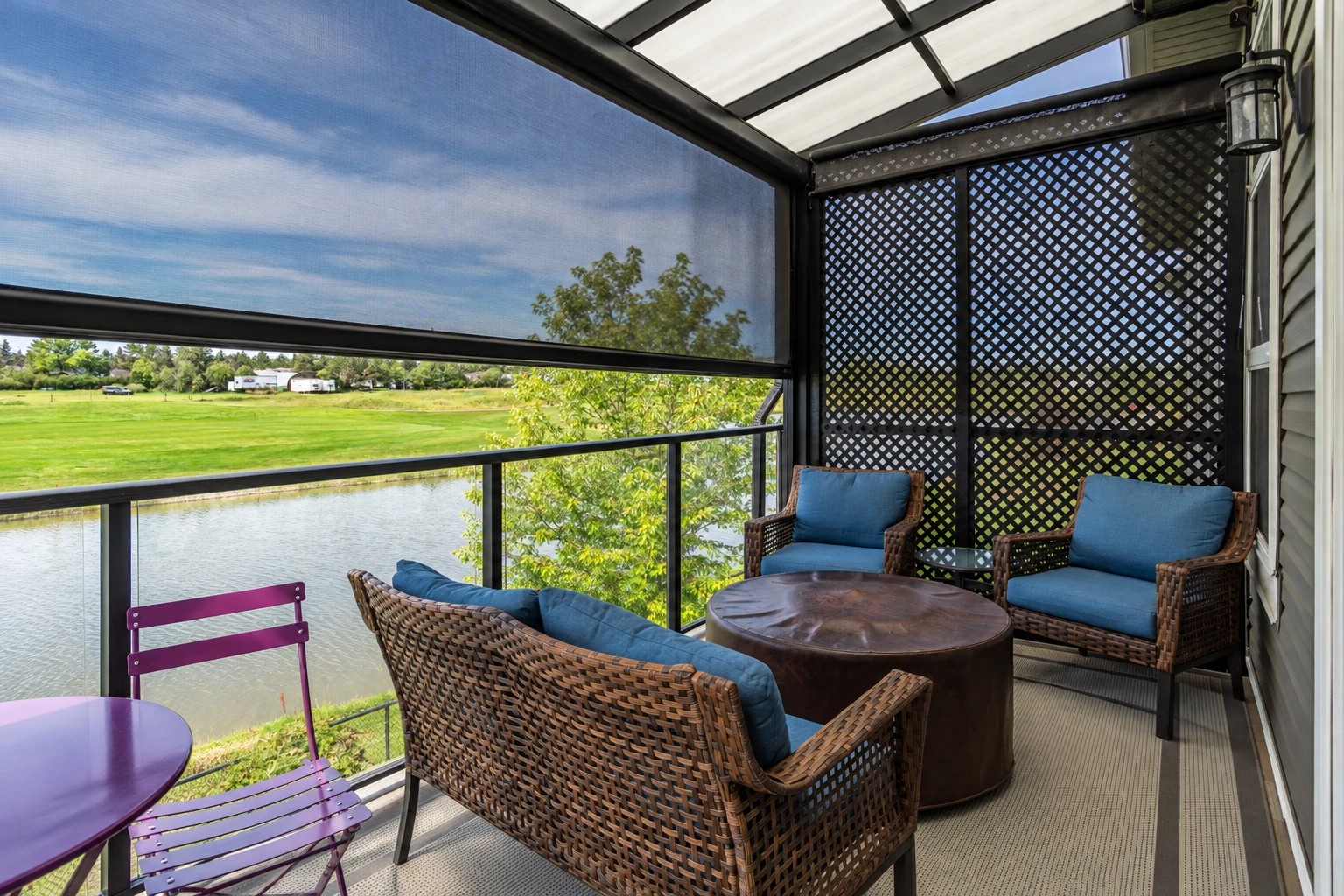 Enclosed patio with a retractable mesh shade, lattice panels, and wicker seating overlooking a pond.