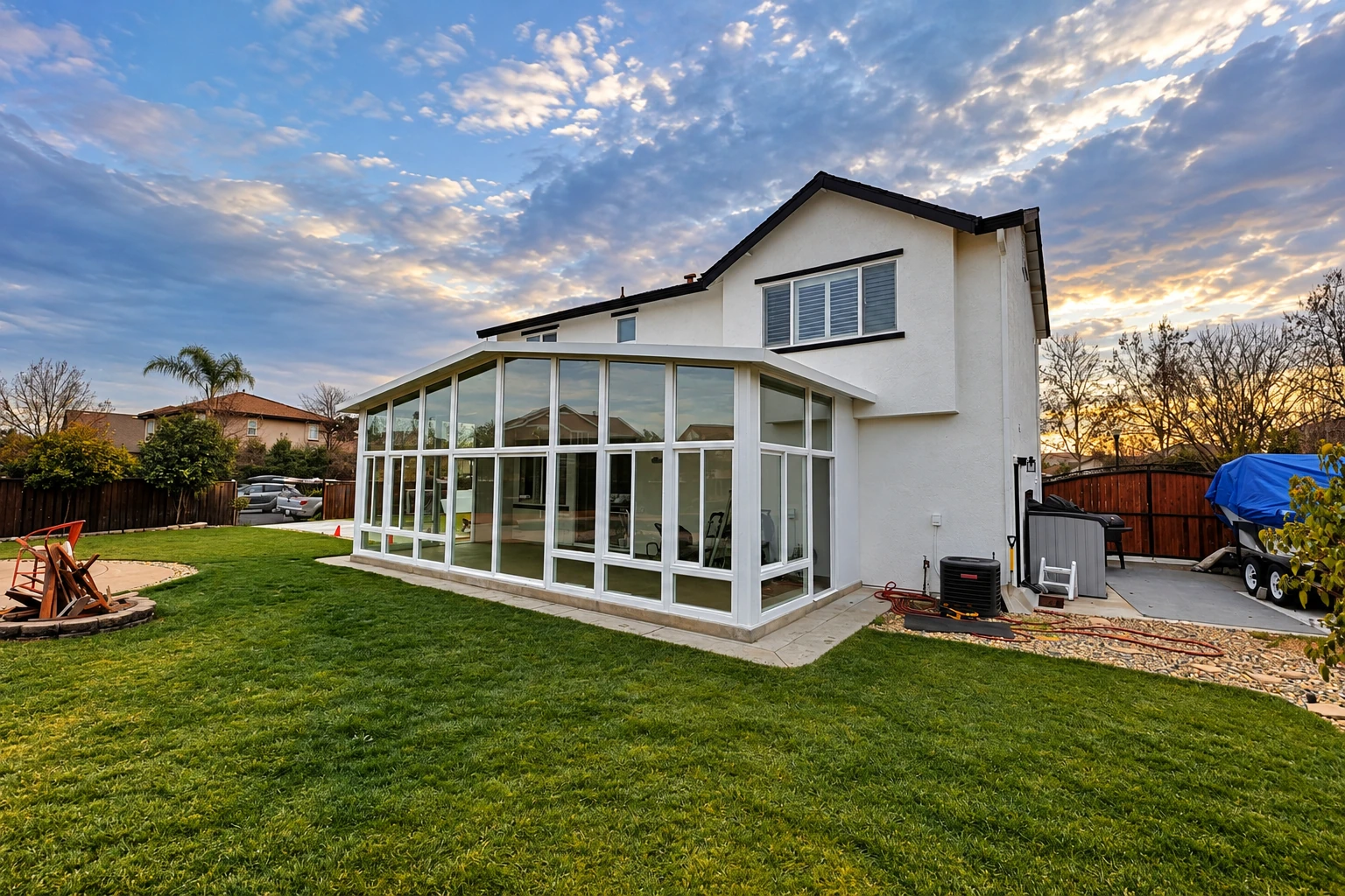 White-framed glass sunroom addition attached to a house, set on a lawn beneath a cloudy evening sky.
