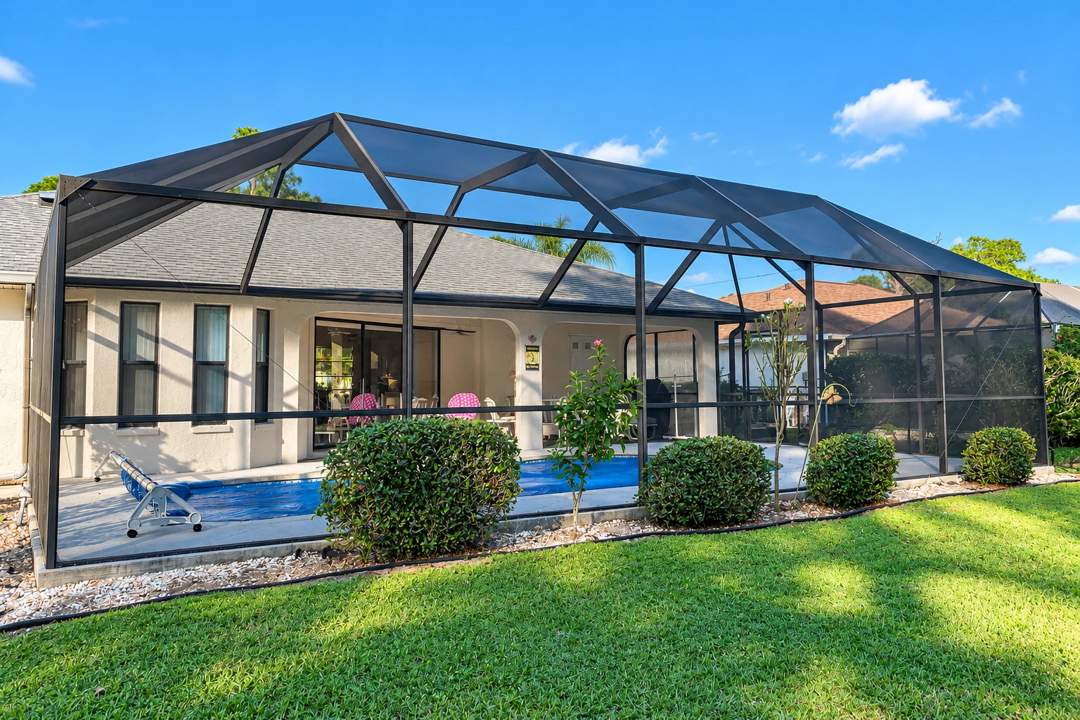 Large black-framed screen enclosure covering a backyard pool and patio behind a single-story home.