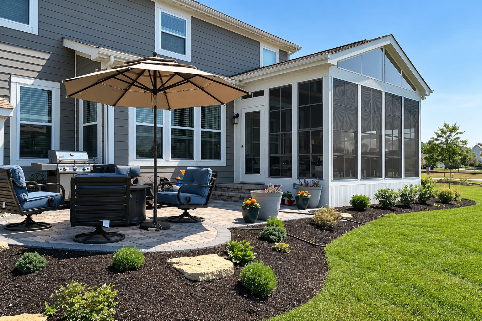 Three-season sunroom with tall screened windows attached to a gray-sided house beside a paved patio.